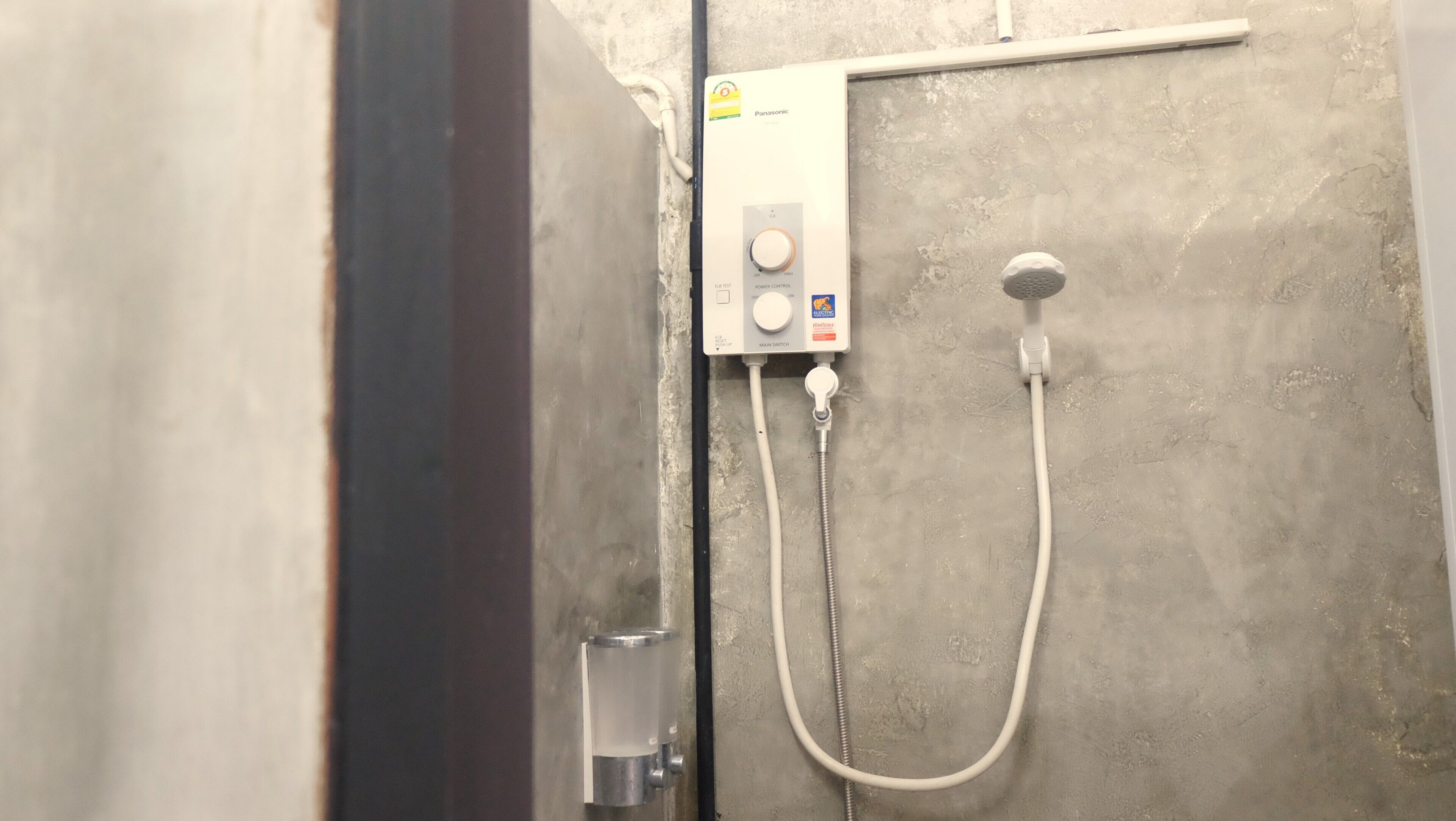 Une salle de bain équipée d’un panneau de commande pour la douche, d’un pommeau de douche à main et d’une tuyauterie visible.