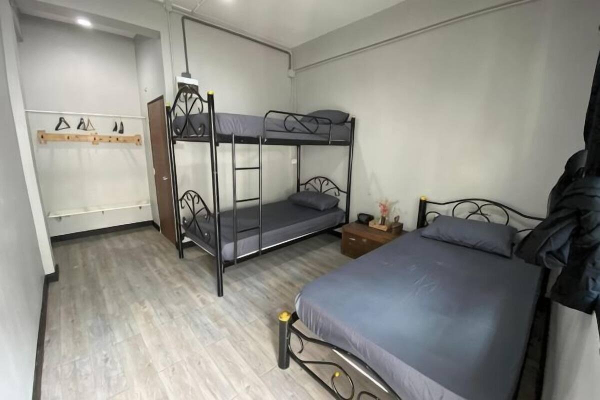 A bunk bed room with a desk and chair, a hanging coat rack, and a wooden door.