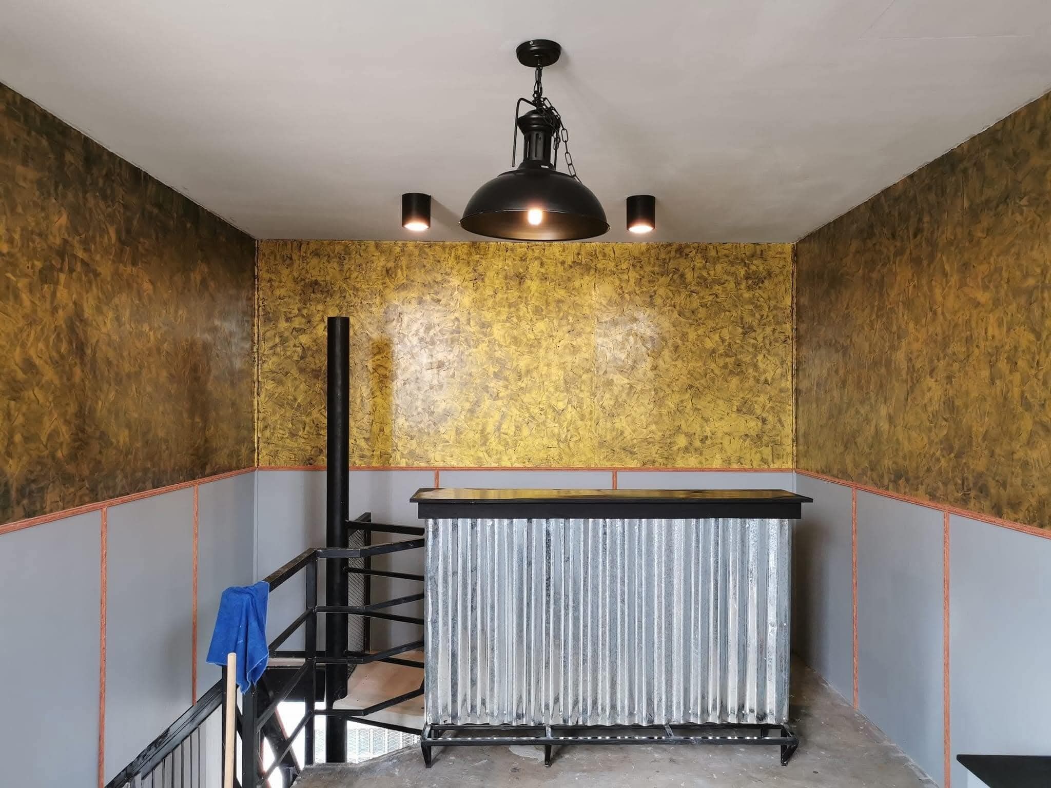 Une pièce avec un radiateur en métal, un escalier orné d’une serviette bleue et un luminaire suspendu noir.