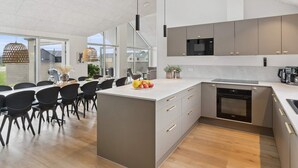 A modern kitchen with a large island, built-in appliances, and a dining area with chairs and a table. - 5 Star Holiday Home in Otterup (Otterup)