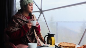 Eine Person sitzt an einem Tisch in einer geodätischen Kuppel und hält eine Tasse. Der Tisch ist mit Tellern, Schüsseln und einer Kaffeekanne gedeckt.