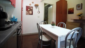 Cocina compacta con estufa a gas, un lavamanos y comedor con una mesa blanca y sillas de metal.