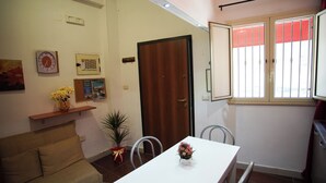 Un pequeño comedor con una mesa blanca, dos sillas, una puerta de madera y una ventana con barrotes.