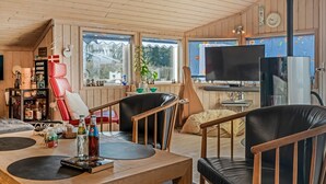 Una sala de estar acogedora con paredes y techo de madera, un televisor, una chimenea y un comedor con mesa y sillas.
