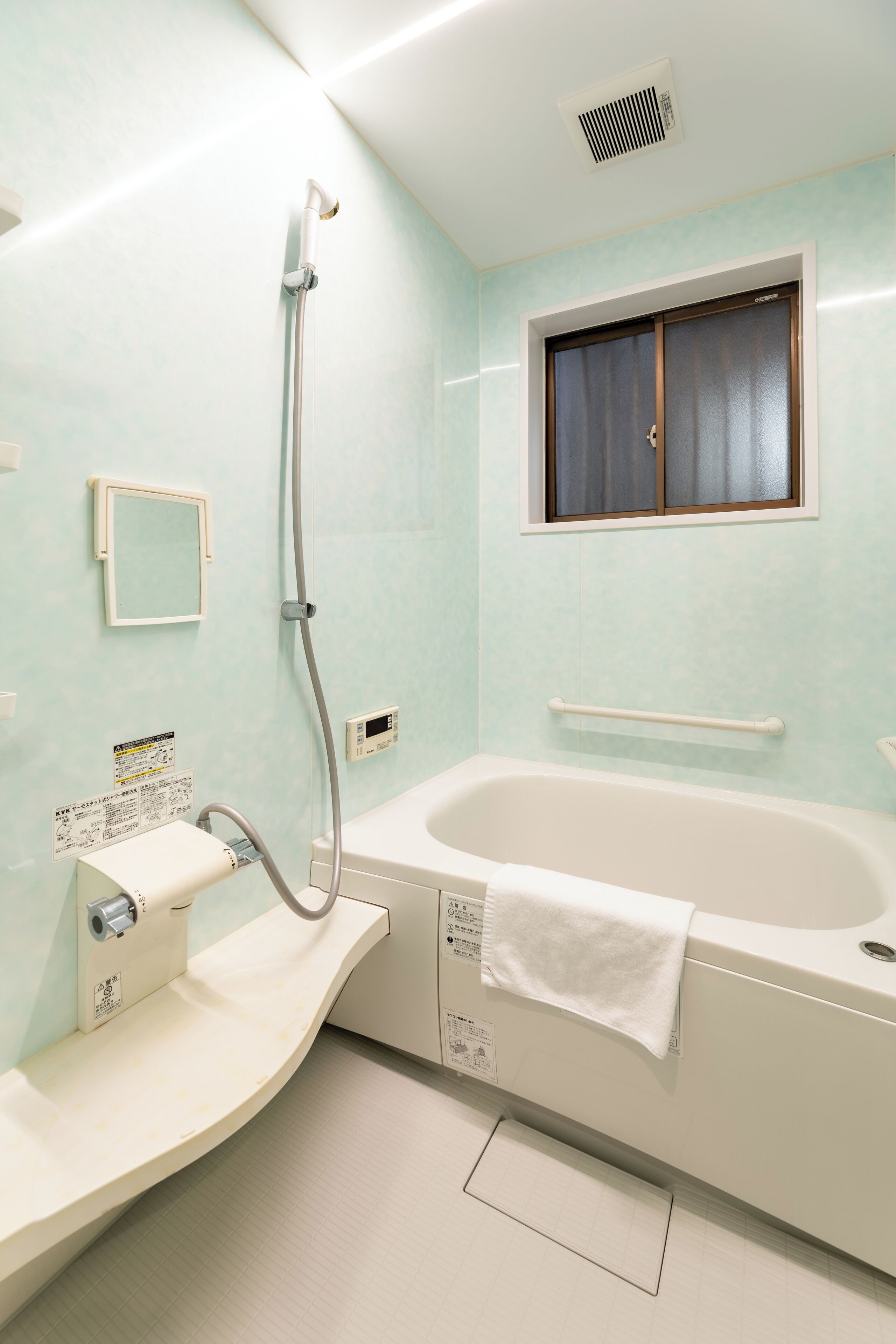 A bathroom with a bathtub, a shower, a window, and a handrail.