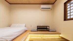 A small, well-lit room with a bed, a table, and a bench. - HIBIHIKARI Tsuruhashi (Osaka)