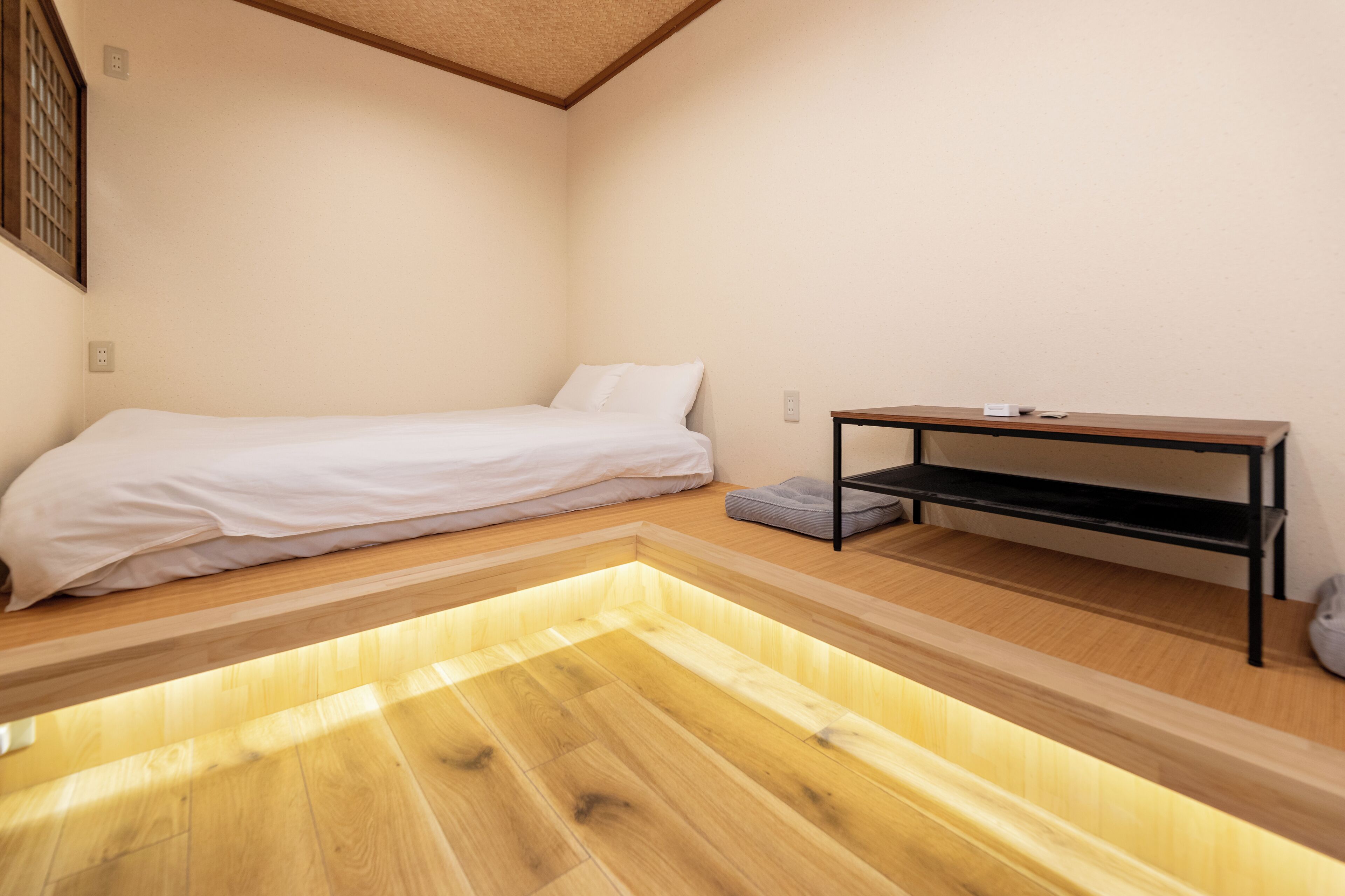 Une petite pièce bien éclairée, avec un lit simple, un banc en bois et une petite table.
