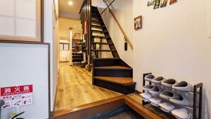A staircase leading to a second floor, a fire extinguisher sign, and a shoe rack with multiple pairs of shoes. - HIBIHIKARI Tsuruhashi (Osaka)
