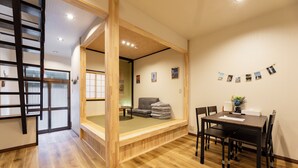 A traditional Japanese-style room with tatami flooring, a low wooden table with chairs, a futon bed, and a sliding door leading to another room. - HIBIHIKARI Tsuruhashi (Osaka)