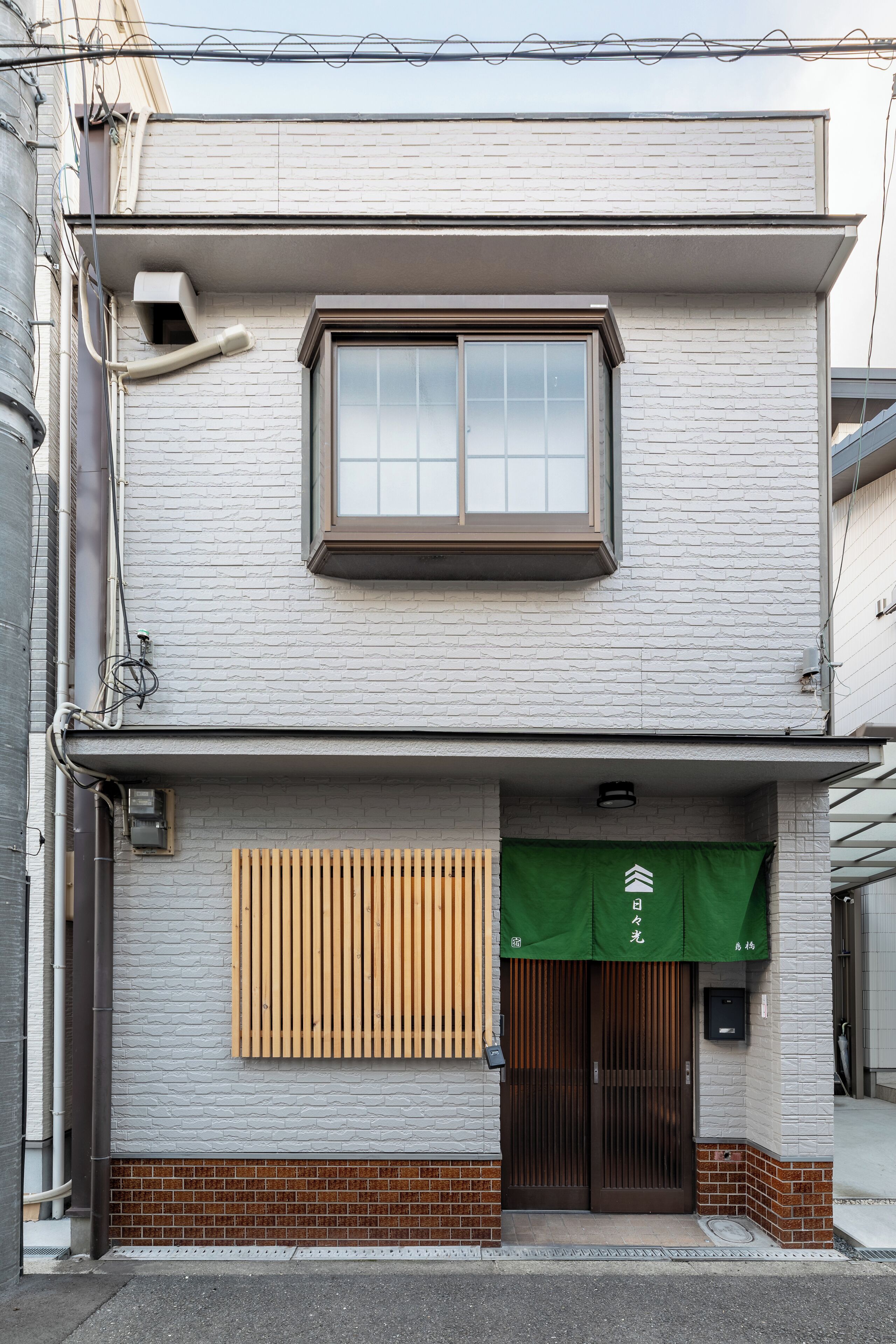 Een gebouw met twee verdiepingen, met een groot raam op de bovenverdieping en een groen luifel met Japanse tekens.