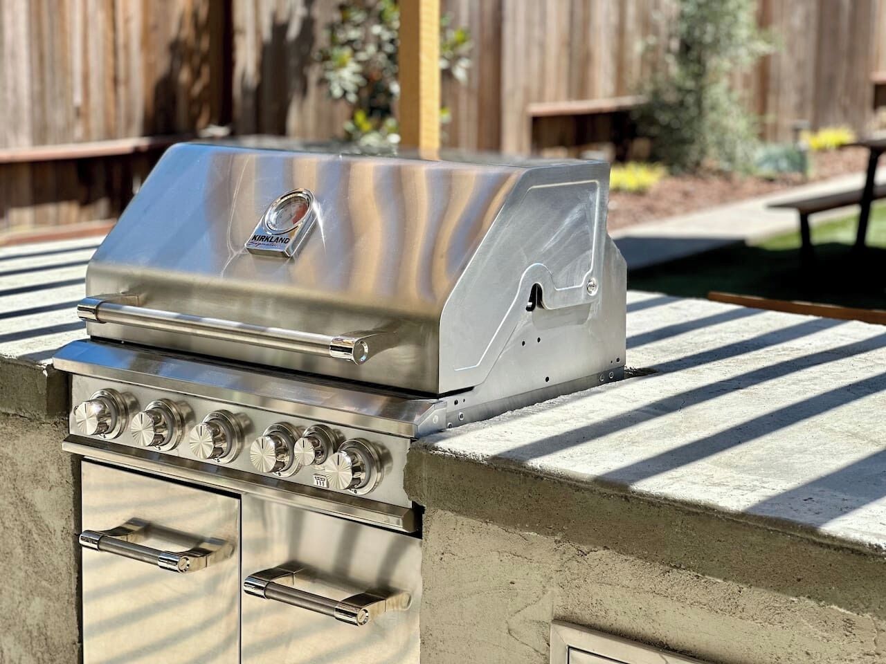 A stainless steel outdoor grill with a lid, a control panel with knobs, and a vent.