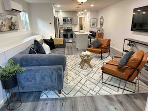 A modern living room with a sofa, armchairs, a coffee table, and a kitchen in the background.