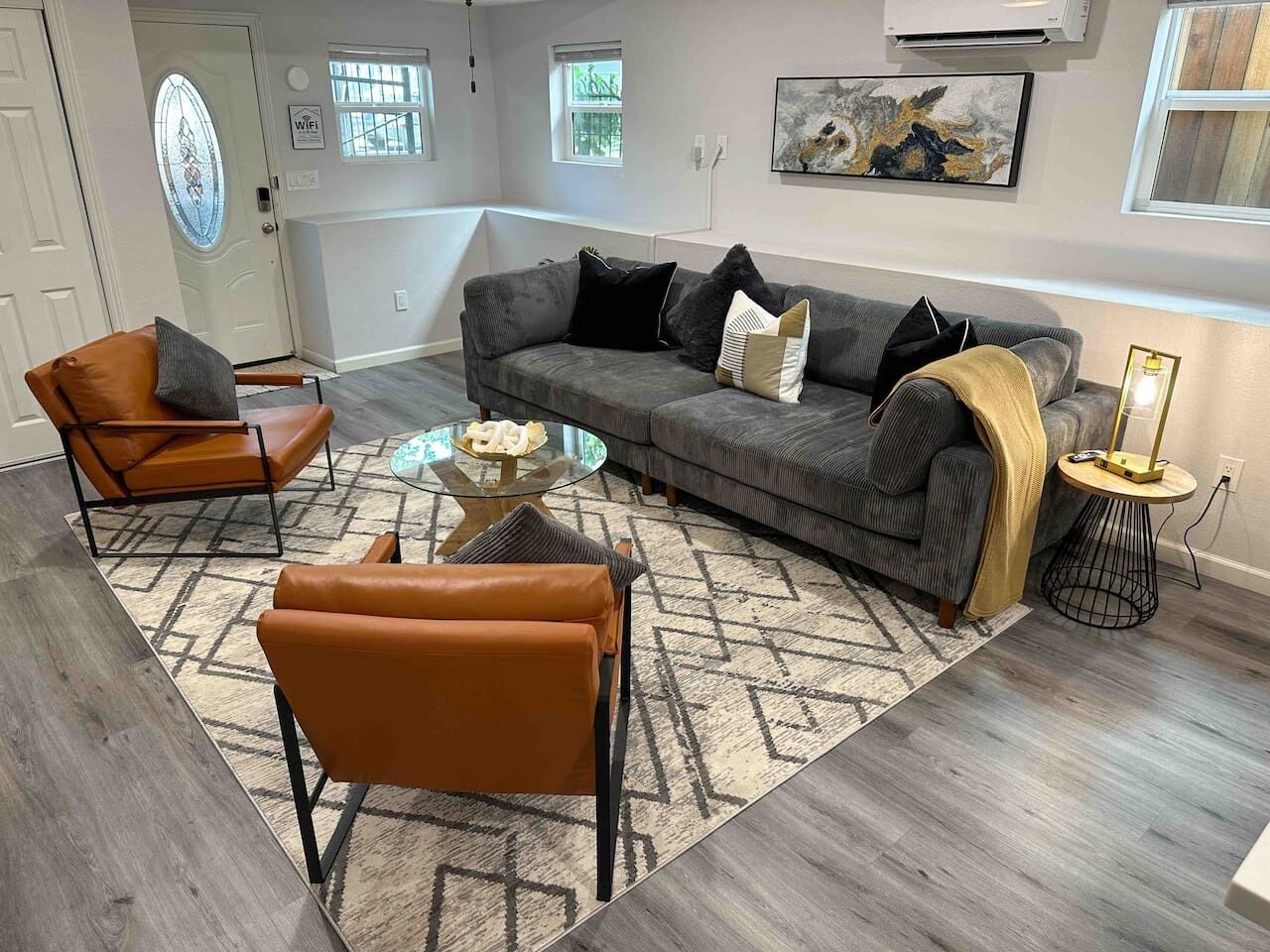Un salon avec un canapé gris, deux fauteuils en cuir marron, une table basse en verre et un tapis à motifs.