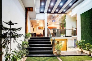 A modern hotel lobby with a staircase, indoor plants, and a green wall.