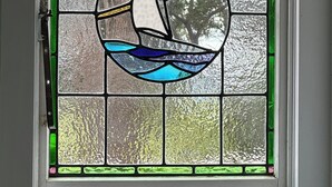 Ein Fenster mit einer Blei-Glas-Einlage, die ein Segelboot auf dem Wasser zeigt.