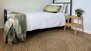 Ein ordentlich eingerichtetes Schlafzimmer mit einem Bett, einem Nachttisch mit Pflanze und einem gewebten Teppich.