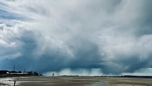 Ein stürmischer Himmel über einer ebenen Landschaft mit einem entfernten Gebäude.