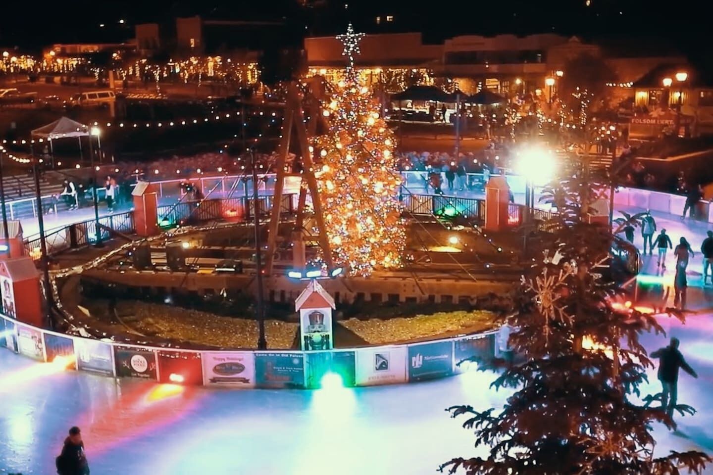 A circular outdoor area with a central tree decorated with lights, surrounded by a fence and various structures.