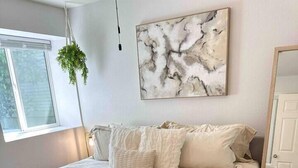 A bedroom with a large bed, a hanging plant, a marble artwork, and a view of the outdoors. - King-Sized Luxury Furnished Space- Downtown Sac! (Sacramento)