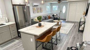 A modern kitchen with a central island, bar stools, a refrigerator, and a dining area with a sofa and chairs. - King-Sized Luxury Furnished Space- Downtown Sac! (Sacramento)