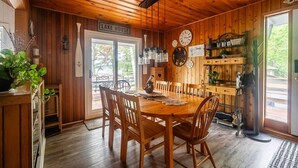 Ein Holzinnenraum mit Esstisch, Stühlen, einer Uhr und einem Schild mit der Aufschrift 'LAKE HOUSE'.