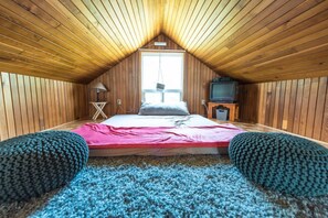 Une chambre avec un plafond en pente, un lit avec un matelas rose, une télévision et une fenêtre.