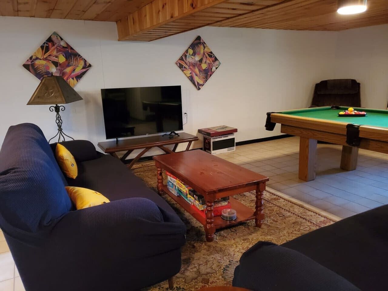 A living room with a sofa, a coffee table, a pool table, a television, and decorative wall art.