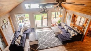 Ein geräumiges Wohnzimmer mit hoher Decke, Deckenventilator und großem Fenster mit Blick auf eine Terrasse.