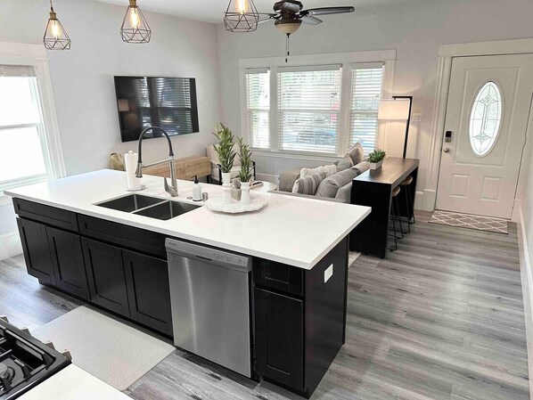 Une cuisine moderne dotée d’un îlot central, de meubles de couleur noire, d’appareils électroménagers en acier inoxydable et de luminaires suspendus.