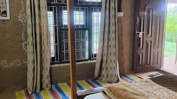 Una habitación con una cama, una ventana con barrotes, una cortina, una lámpara en la pared y una puerta.