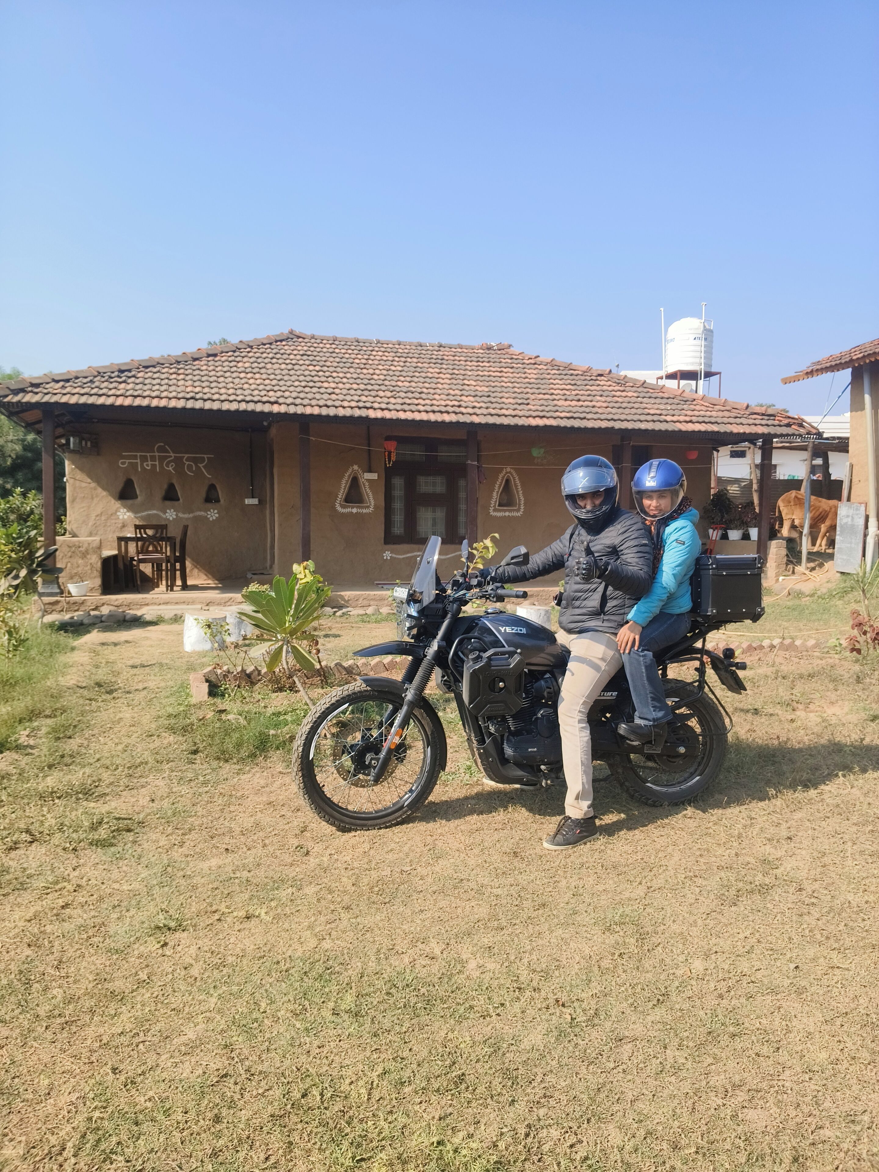 A motorcycle parked in front of a rustic building with a tiled roof and a water tank on the roof.