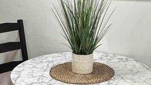 Een ronde marmeren tafel met een geweven placemat, een potplant en een zwarte stoel.