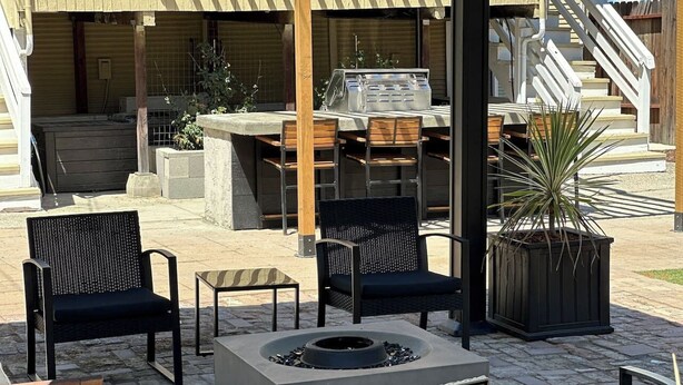 Een terras buiten met een barbecue, stoelen en een vuurkuil.