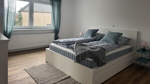 Een slaapkamer met een bed, een raam met gordijnen, een nachtkastje en een radiator.