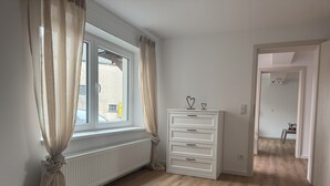 Een kamer met een groot raam, een witte lade en een houten vloer.