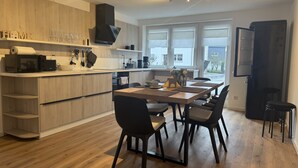 Een moderne keuken met houten kastjes, een eethoek met een tafel en stoelen, en een groot raam dat natuurlijk licht binnenlaat.