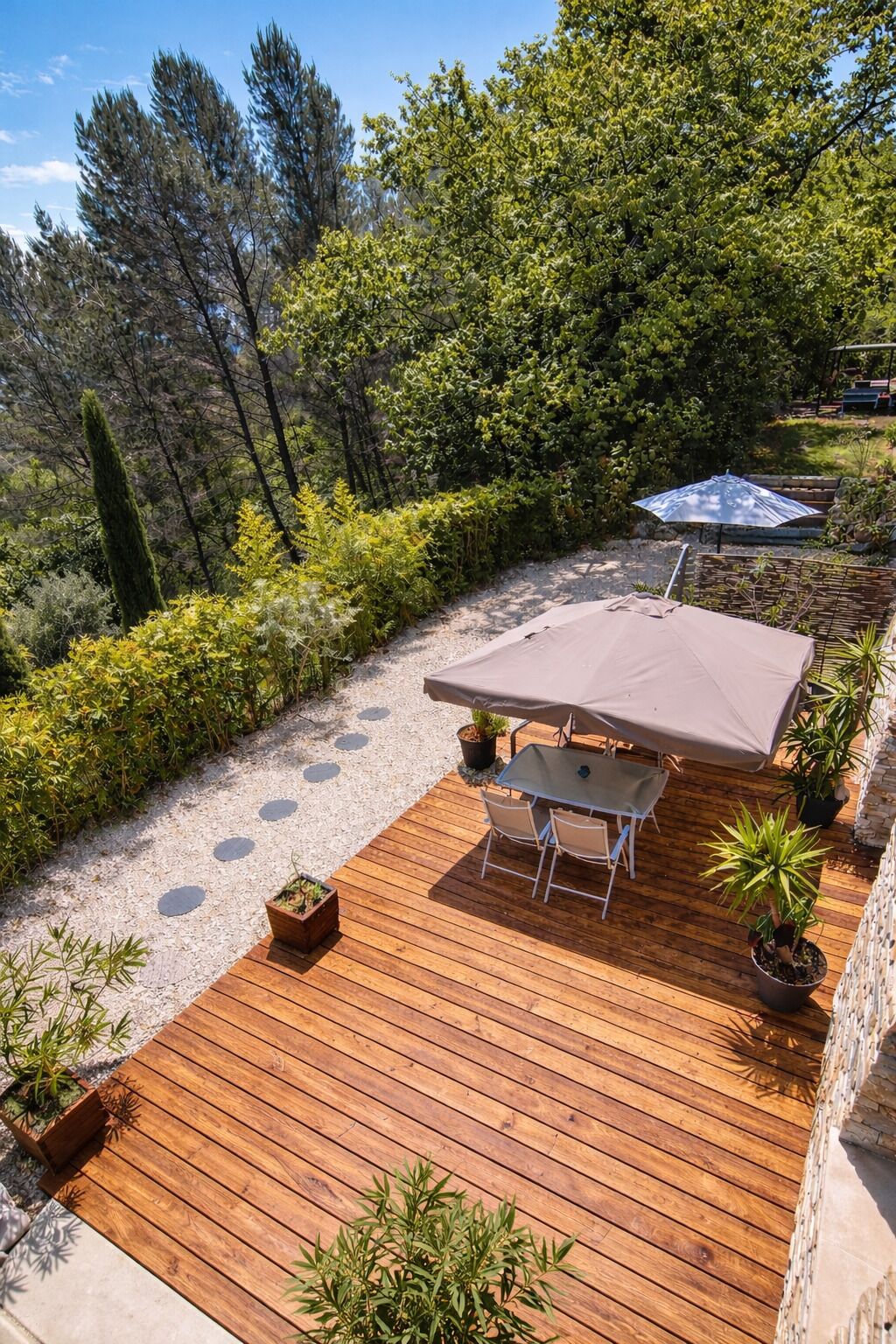 A wooden deck with a table and chairs, surrounded by potted plants and a covered seating area.
