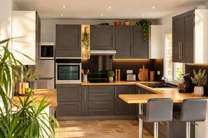 A modern kitchen with dark cabinetry, a built-in oven, a microwave, and a stainless steel range hood. - Comfortable flat – Swimming pool, boules court & peaceful setting in Pertuis (Pertuis)
