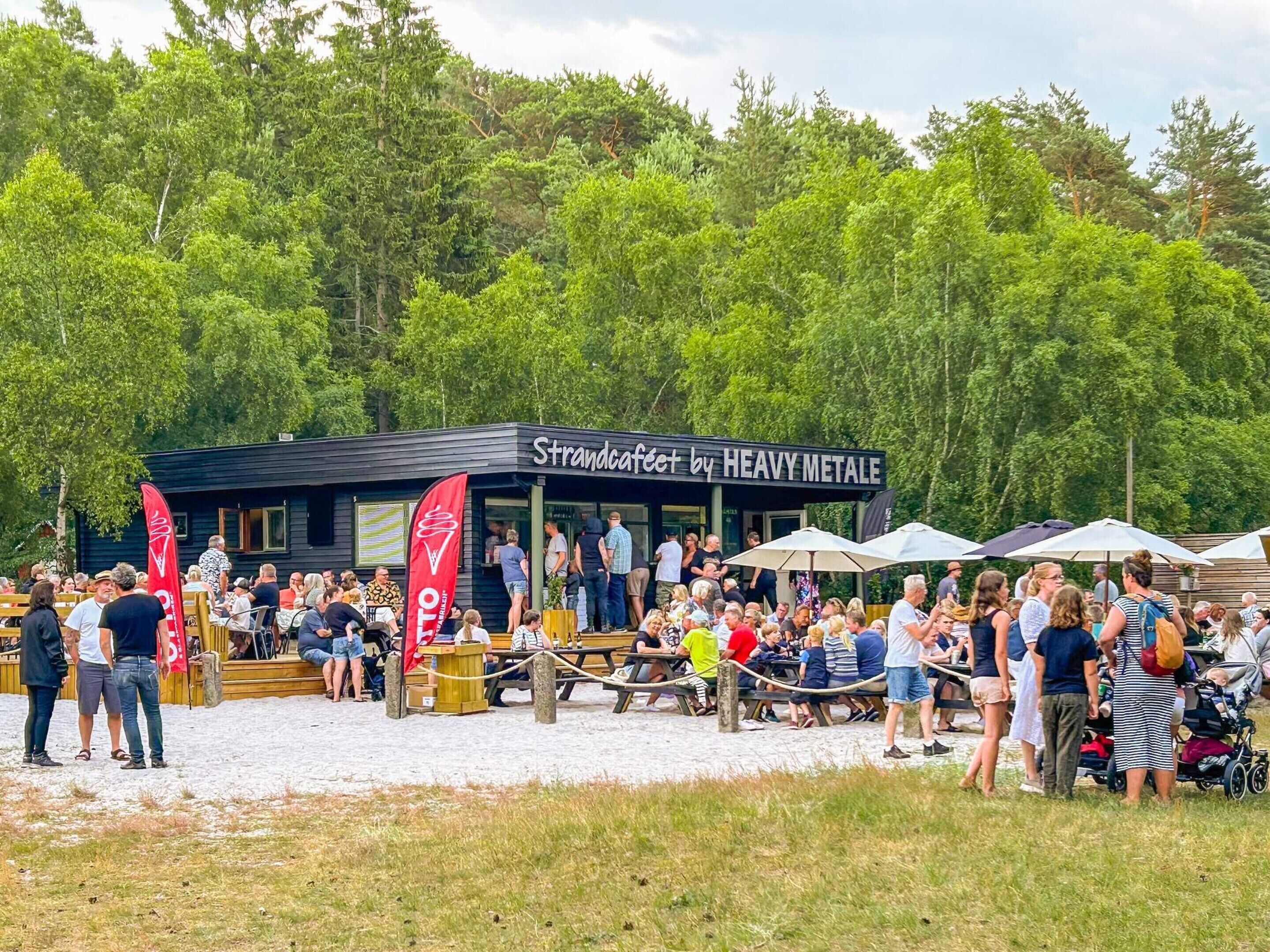 Un restaurante llamado 'Strandcafé by Heavy Metale' con terraza y vistas a árboles.