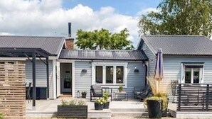 Ein zweistöckiges Haus mit einer Terrasse, einem überdachten Sitzbereich und einem kleinen Garten.