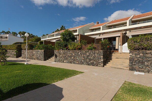 Una casa moderna de dos pisos con fachada de piedra, techo plano y un jardín bien cuidado.