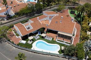 A residential property with a swimming pool, multiple lounge chairs, and a covered patio area.