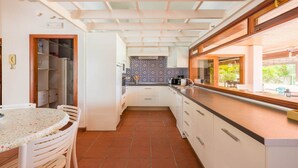 Una cocina con armarios blancos, salpicadero de azulejos y un comedor con una mesa redonda y sillas.