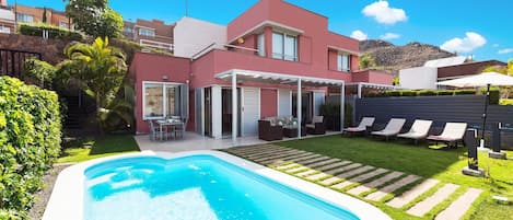 Ein modernes, zweistöckiges Haus mit Swimmingpool, Sitzgelegenheiten im Freien und einem gepflegten Garten.