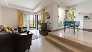 A modern living room with a sofa, TV, and dining area with chairs. - Villa in Salobre Golf with Private Pool (San Bartolomé de Tirajana)