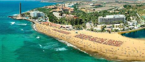 Luftaufnahme eines Küstenresorts mit Sandstrand, einem Leuchtturm und mehreren Hotels.