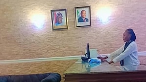 Un mostrador de recepción con una computadora, cuadros enmarcados en la pared, un sofá y una alfombra estampada.