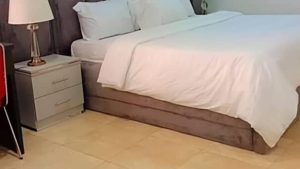 Una cama bien hecha con sábanas blancas, cabecera oscura y dos lámparas de noche.