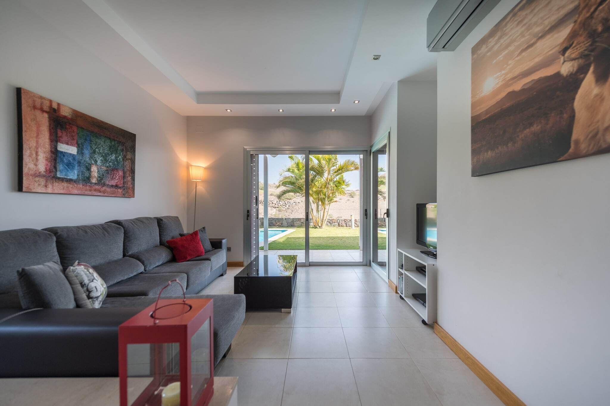 A modern living room with a grey sofa, a red side table, and a large painting on the wall.