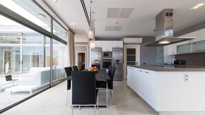 A modern kitchen with stainless steel appliances, a central island, and a dining area with black chairs and a glass table. - Villa in Anfi Tauro near Beach & Golf (Mogán)
